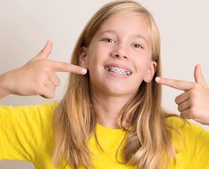 Puntillo and Crane Orthodontics, Treatments, Picture of little girl smiling and pointing to her braces